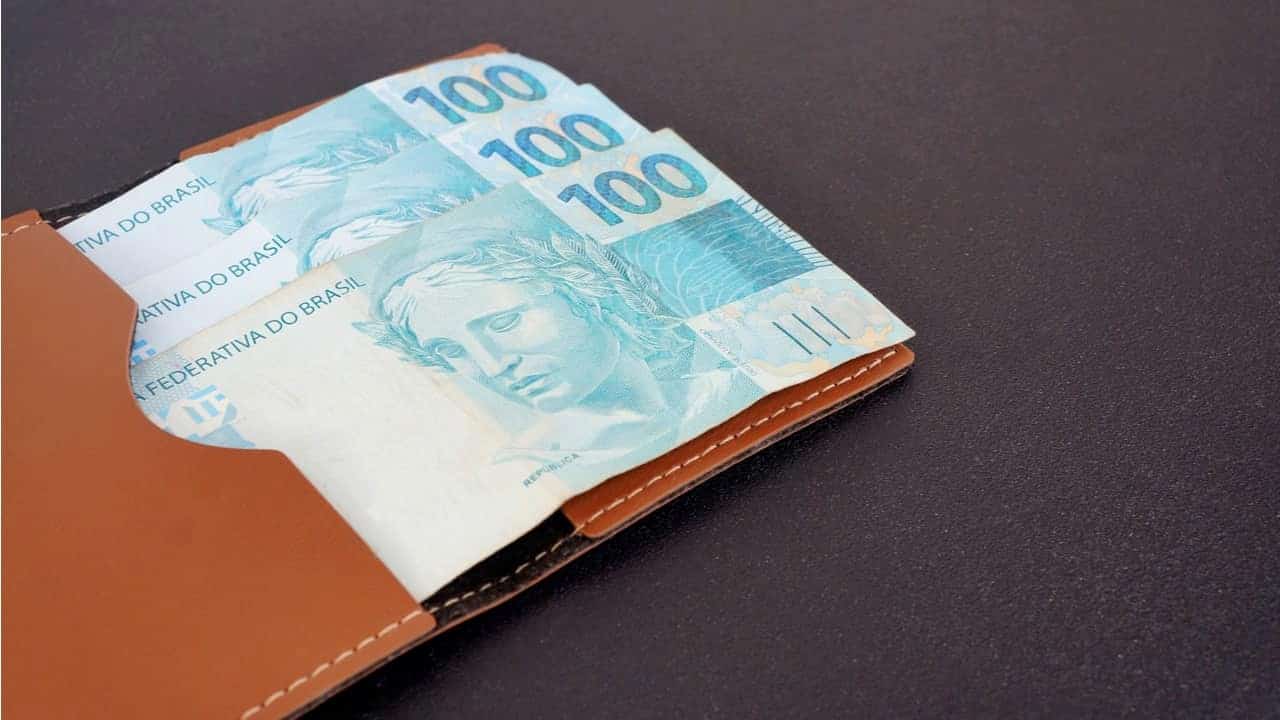 Notas de 100 reais sobre um carteira marrom. renda-extra DINHEIRO