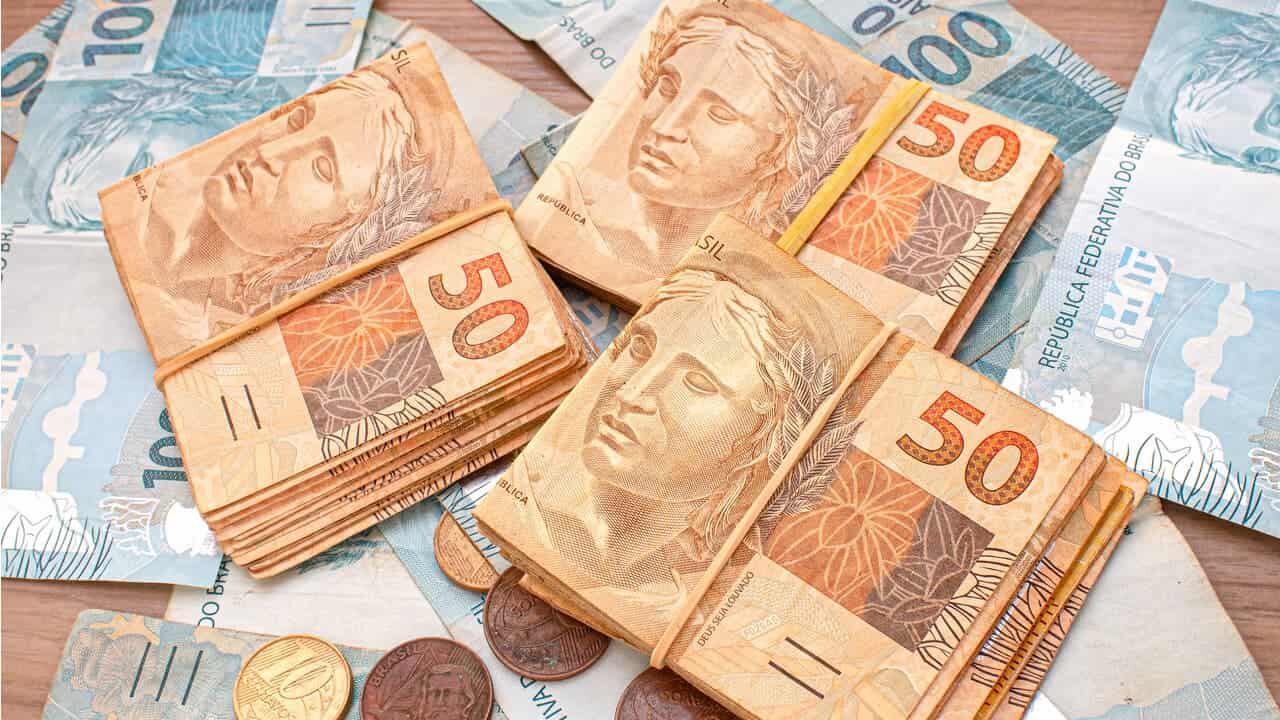 Cédulas de 50 envoltas em elástico amarelo, notas de 100 reais e moedas